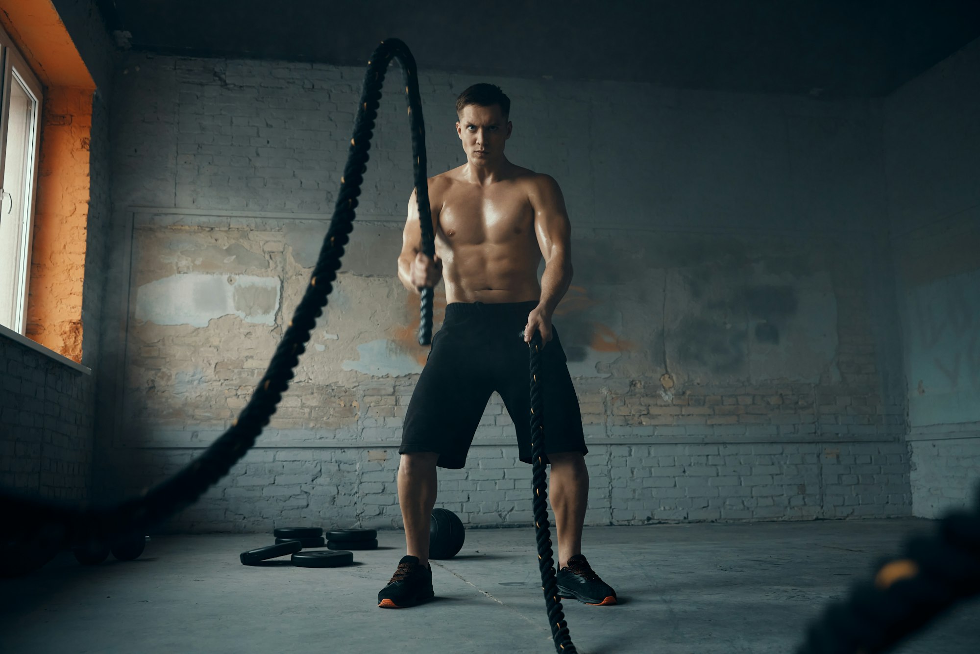 Concentrated young man exercising with battle rope in gym